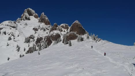 tiro de dron con dos personas escalando lentamente una montaña durante la temporada de invierno