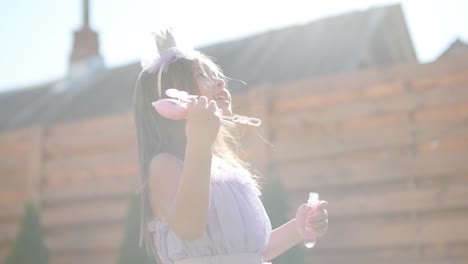 a little girl in a dress is blowing soap bubbles in the backyard on a sunny summer day