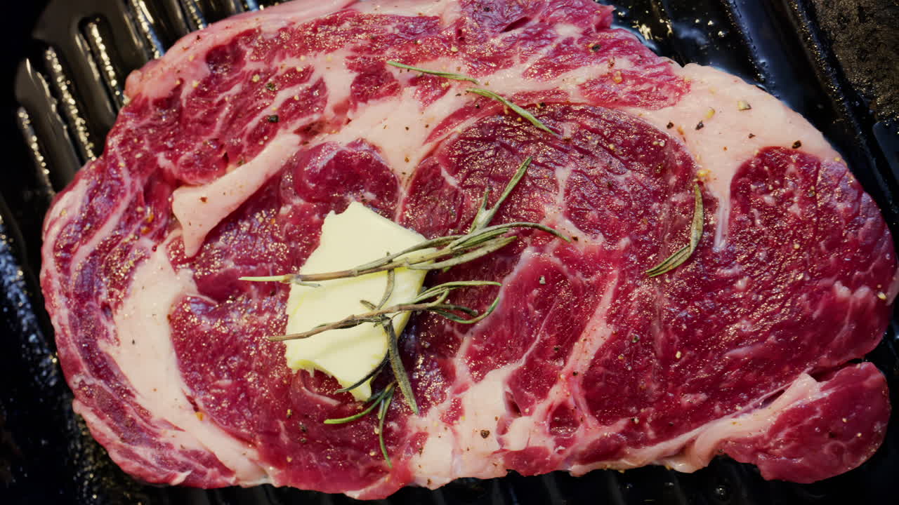 Burro che si scioglie su una bistecca condita che cuoce su una padella griglia calda con rosmarino
