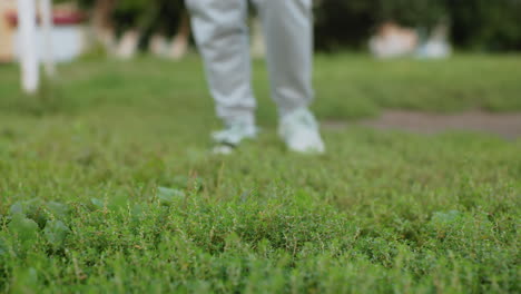 round leg view of sports woman doing squats on green grassy field during outdoor fitness session under bright sky, wearing sportswear and sneakers, showcasing active lifestyle, energy, and health