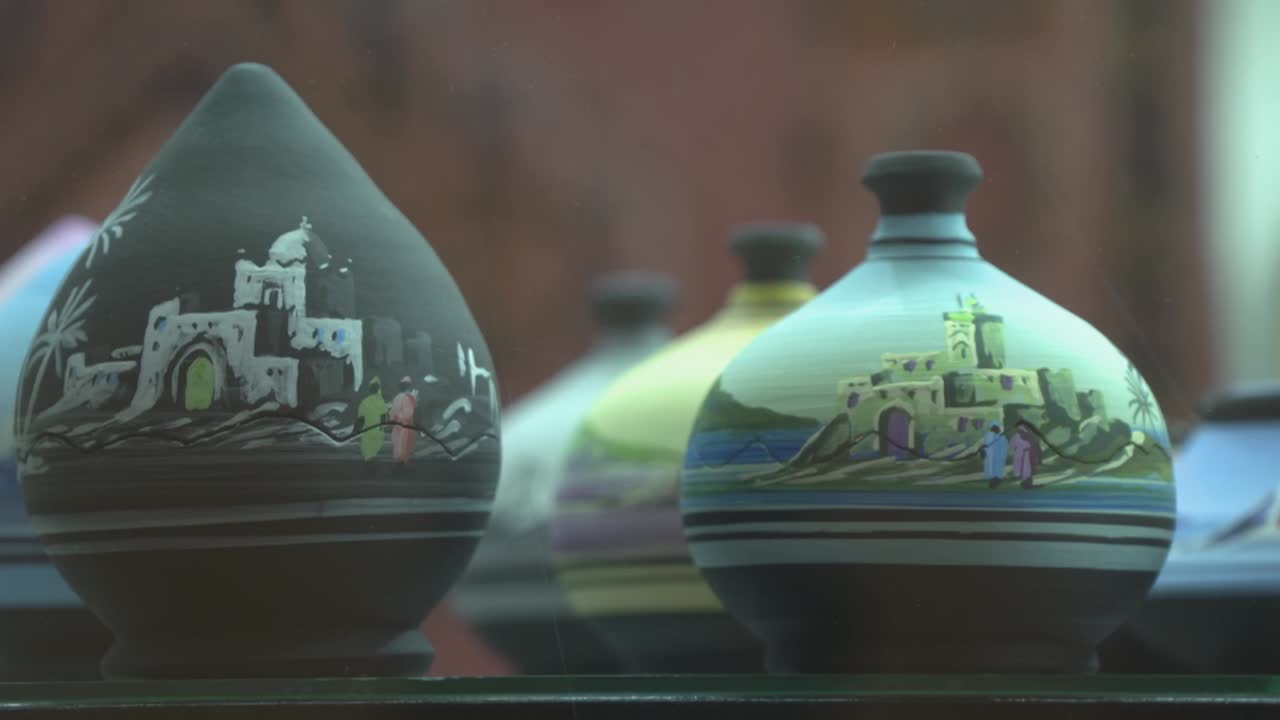 Vue détaillée de poteries artisanales en céramique présentant une architecture marocaine traditionnelle peinte à la main. Les vases présentent des dessins miniatures de bâtiments Kasbah blancs, d’arches et de palmiers.