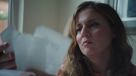 woman looking in despair at receipts and bills, handheld shot in daytime indoors by window