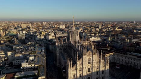 drone reveal milan duomo cathedral in downtown with skyline of the city main european capital during sunset warm light , cinematic aerial footage