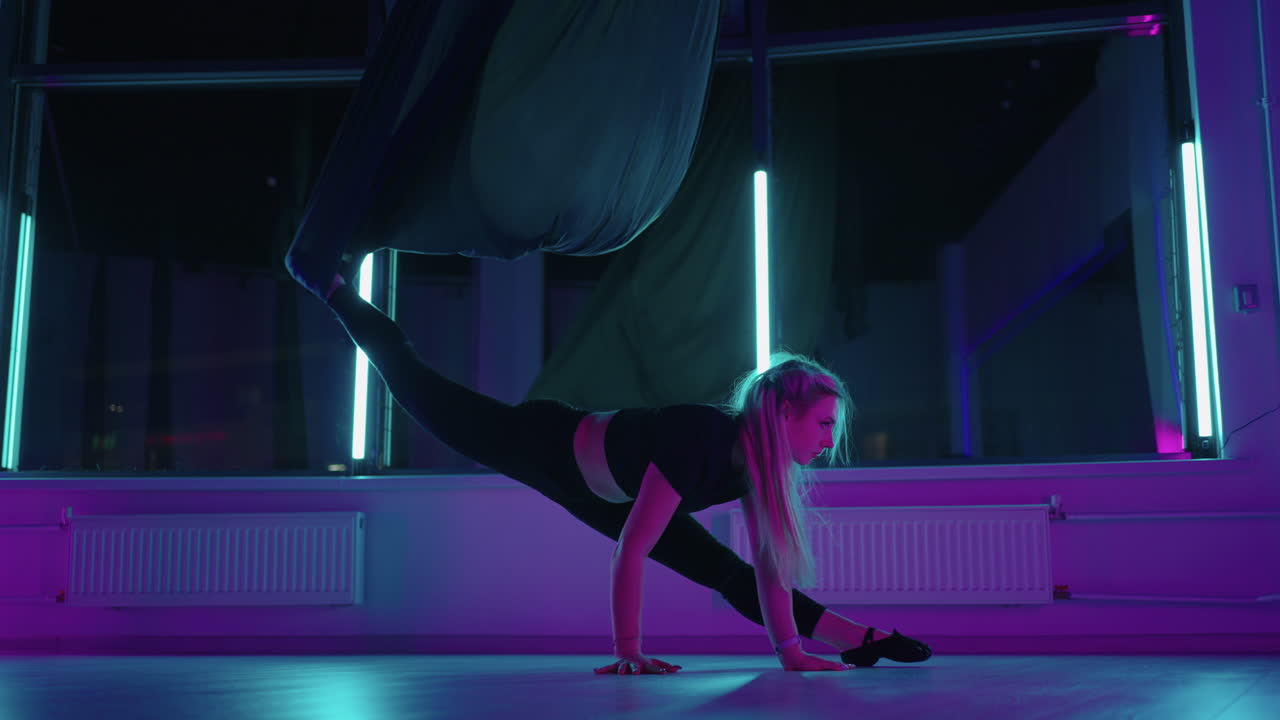 una donna sta facendo esercizi di allungamento in una lezione di yoga aerea usando un'amaca per allenare il suo corpo