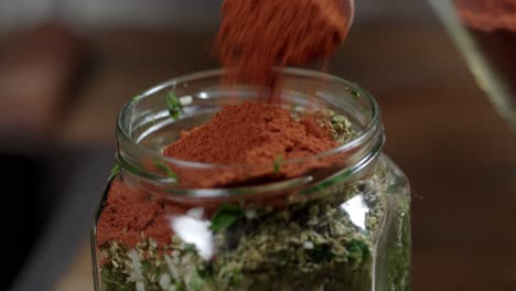 adding red pepper with a spoon to the chimichurri sauce in the glass container where it is kept