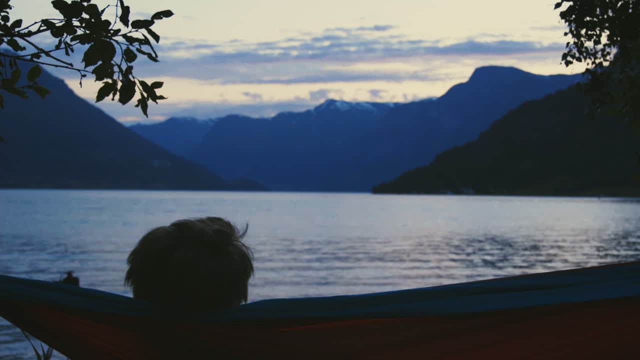 그의 해먹에서 일몰을 즐기는 젊은 남자의 실루엣