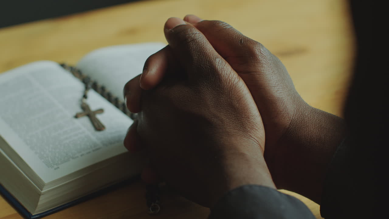 Clasped Hands of Clergyman Leaning on Table with Opened Bible as Praying