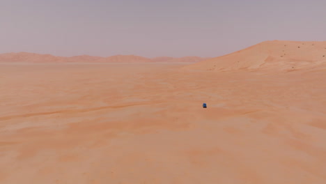 vast desert landscape with a lone blue vehicle in the empty quarter, oman