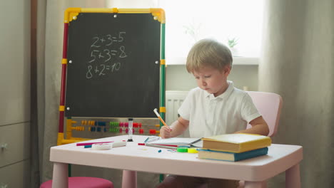 little boy does difficult homework sitting near blackboard