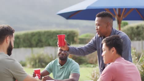 Fröhliche,-Vielfältige-Männliche-Freunde,-Die-An-Sonnigen-Tagen-Im-Garten-Reden-Und-Bier-Trinken