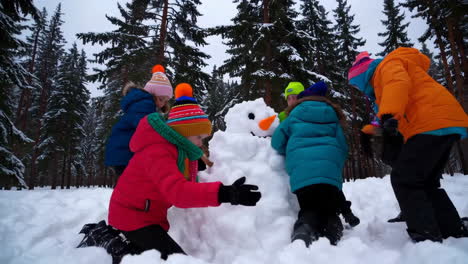 children building a snowman in a snowy winter forest