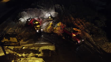 excavators are loading dump trucks with crushed stone and gravel at night