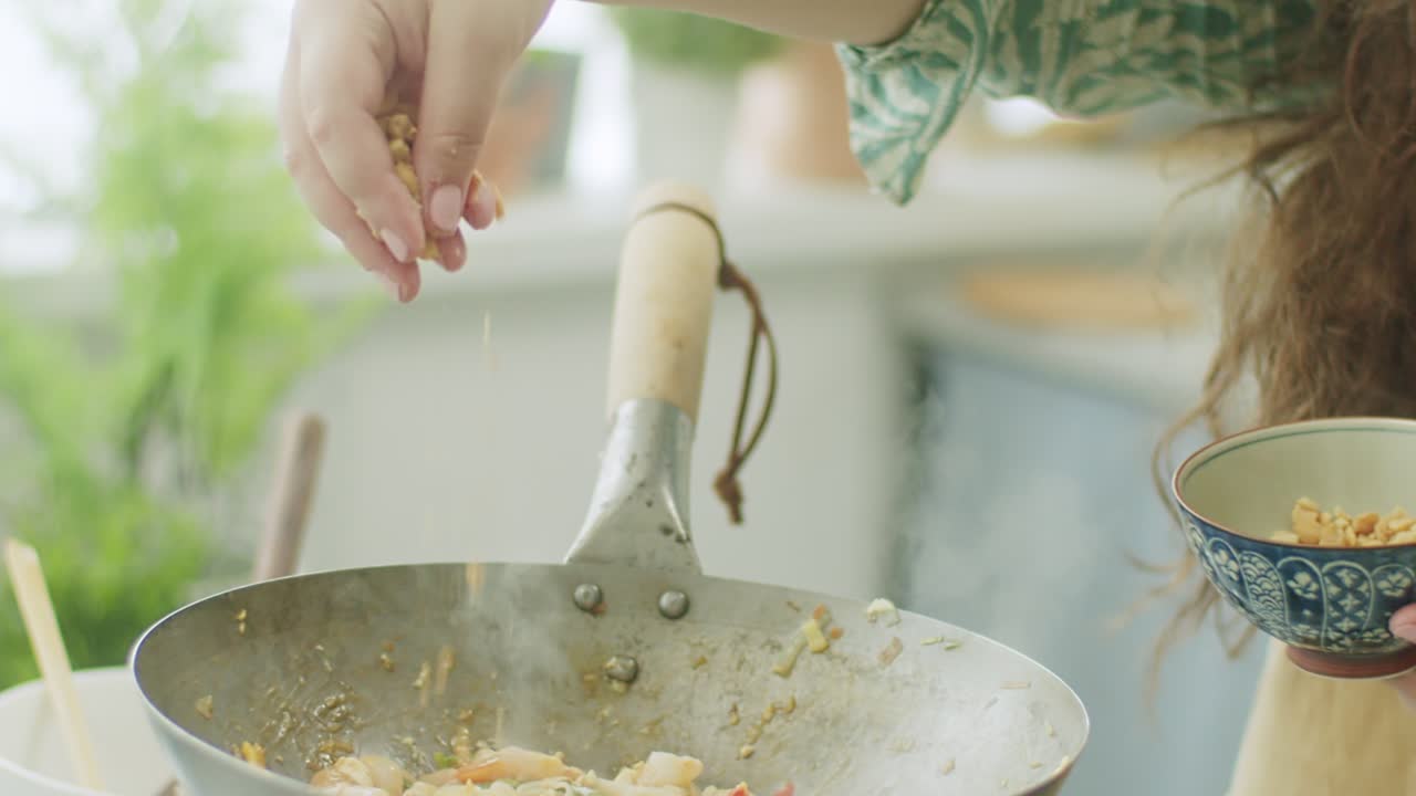 Woman adding peanut to frying pan with wok