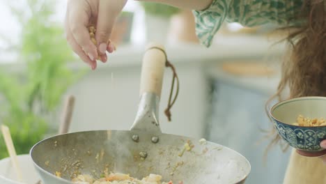 woman adding peanut to frying pan with wok