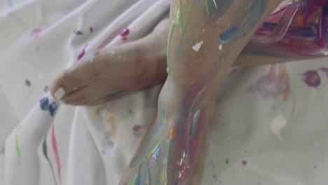 close up of a woman's feet and legs, covered in fresh colorful paint all over her body