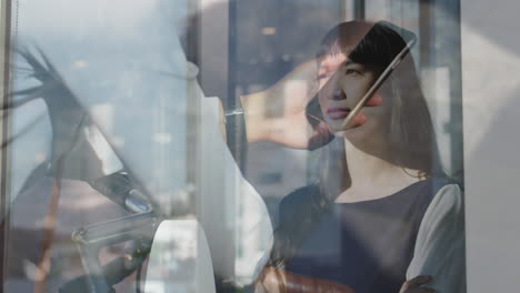 talking on smartphone, businesswoman standing with cityscape reflections in office