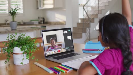 Schoolgirl-using-laptop-for-online-lesson-at-home,-with-her-school-friend-and-web-chat-on-screen