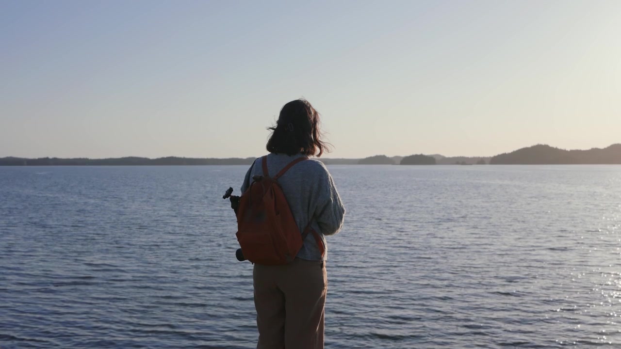 Woman with backpack enjoying calm sea view at sunset