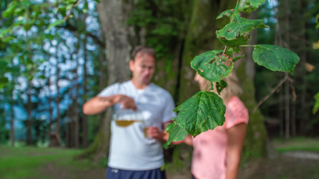 Attractive Married Couple Drink Iced Tea Under Large Tree In Outdoor Park