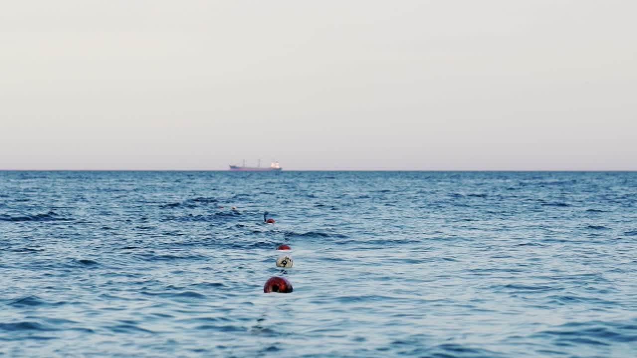 Sea water background with buoys zone. Ship is floating on far distance water on the sea. Blue sea water in the evening under the clear sky.