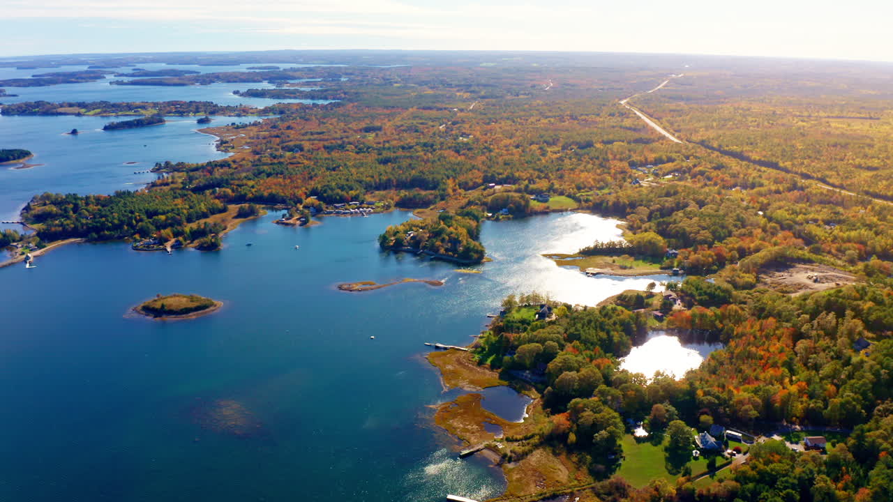 Aerial drone shot over the coastline of Oak Island, Nova Scotia, Canada.
High view of the sea, autumn colorful trees foliage. Picturesque landscape. Fall vibrant colors.