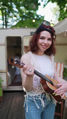 young woman playing ukulele outdoors near a camper van