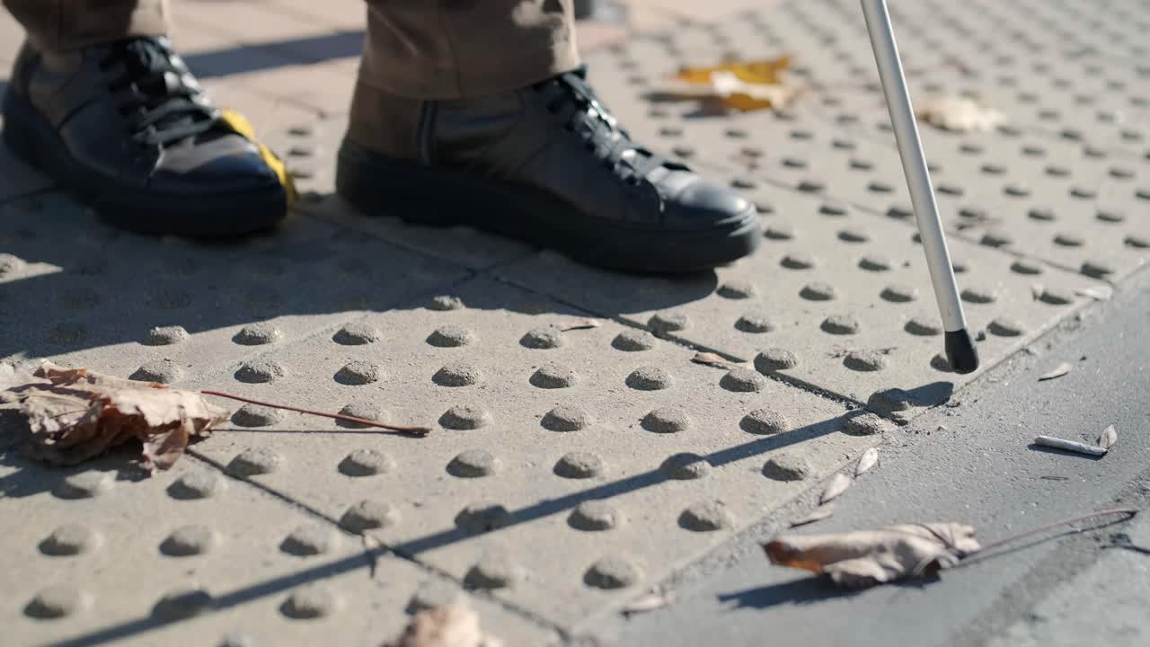 Synshandicappet mand går på en taktil advarselsflise med hjælp fra sin stok. Taktil advarselsflade for synshandicappede udendørs i byen