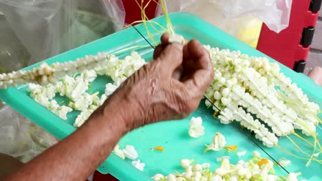 hands threading jasmine flowers into garlands