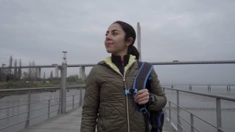 Happy-brunette-hindu-woman-with-backpack-walking-on-wooden-jetty