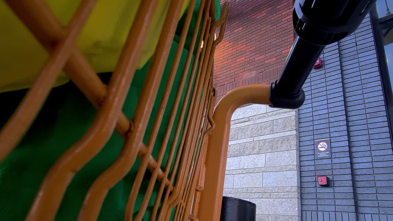 2-2번 출구 옆 야외 주차장에서 하나의 녹색 소포와 다른 하나의 노란색 자루 하역 품목이 있는 쇼핑몰 외부의 호박색 금속 쇼핑 카트