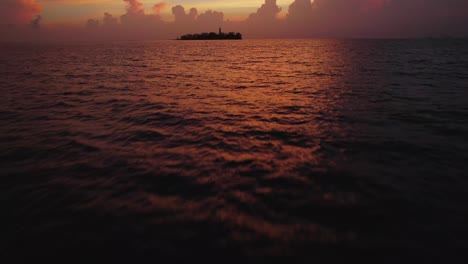 Flying-through-the-ocean-at-sunrise-with-a-tropical-island-as-background