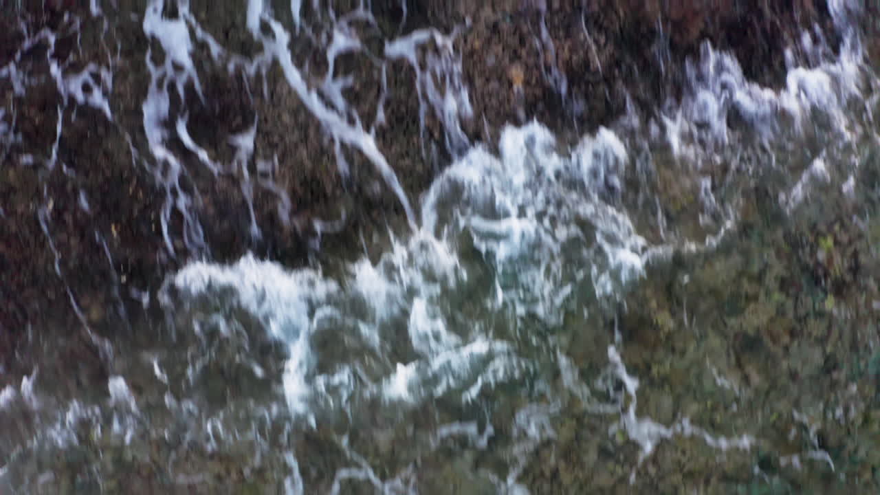 Low flyover ocean waves foaming and crushing on shore with colorful coral rock