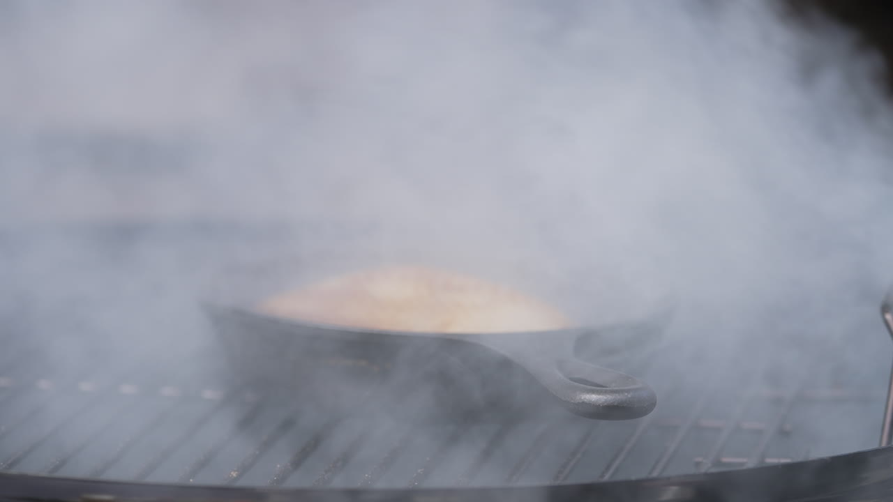 내부의 작은 팬에 김이 나는 음식이 있는 바비큐 그릴에서 연기가 발생합니다.