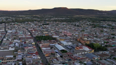 Drone-moving-towards-the-center-of-Jerez,-Zacatecas,-showcasing-Rafael-Paez-garden,-the-parish,-and-the-sanctuary-in-the-distance