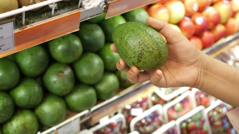 persona con un aguacate en una tienda de comestibles