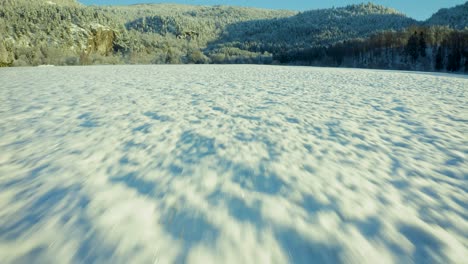 aerial dolly over empty snow covered field with beautiful winter forest landscape up along hills, space for text