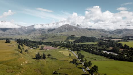 hiperlapso aéreo de tierras de cultivo y una carretera al pie de una impresionante cadena montañosa con nubes bajas arriba