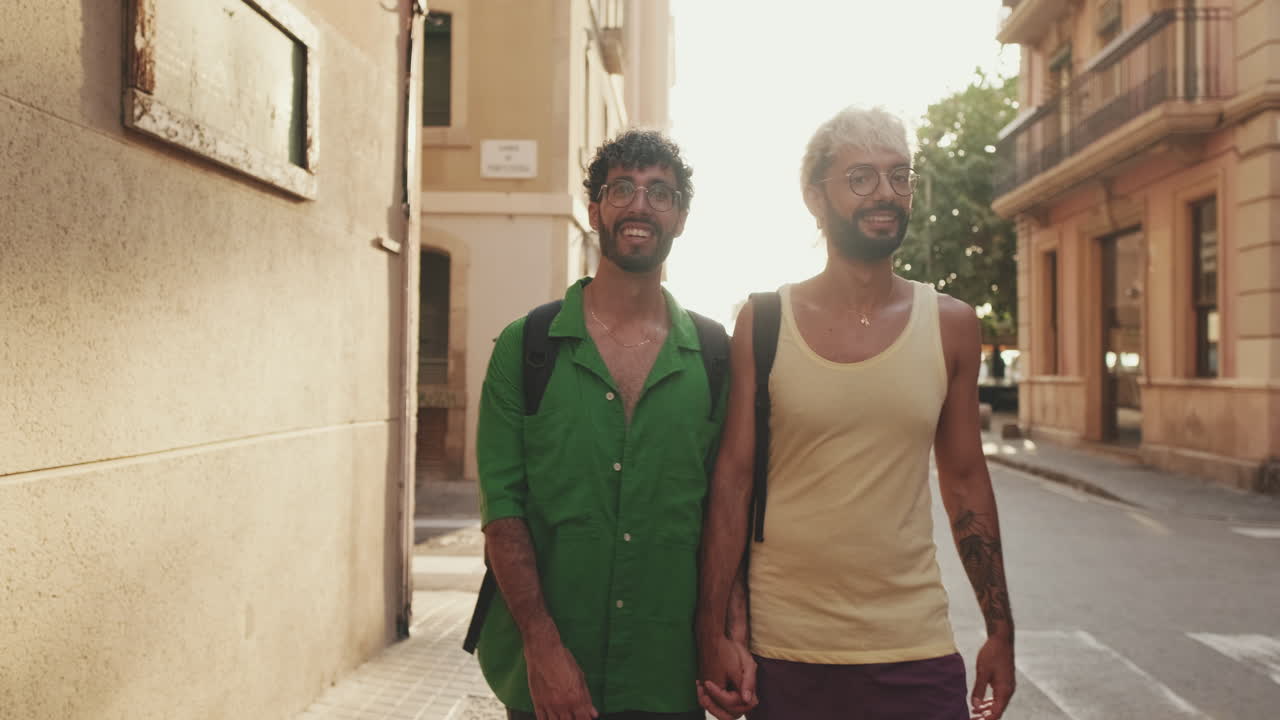 Šťastný gay pár procházející se ruku v ruce po slunné městské ulici.