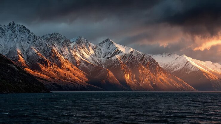 Majestic Mountain Landscape Under Dramatic Skies Showcasing a Stunning Contrast of Snow-Capped Peaks and Lush Water Below During a Quiet Moment in Nature's Splendor