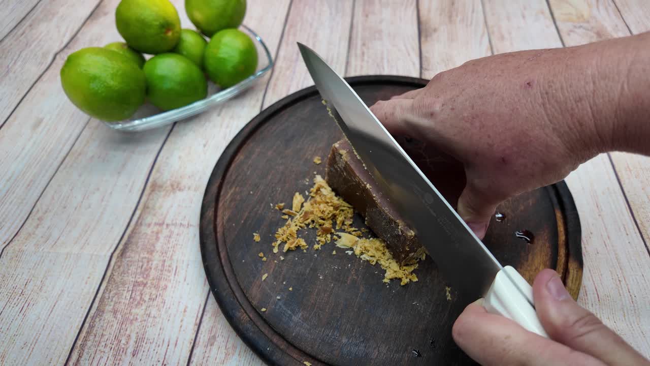 Hand cutting panela with knife on wooden board beside fresh limes