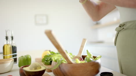 a mature caucasian woman preparing salad in bright kitchen