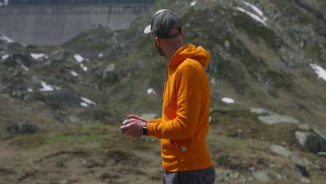 Adult-Male-Wearing-Orange-Hoody-And-Baseball-Cap-Looking-At-Drone-Controller-Unit-As-He-Pilots-Craft