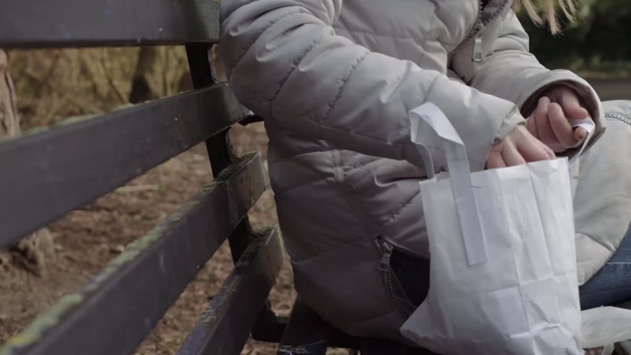 Woman with healthy packed lunch of sandwich and orange juice on park bench medium shot