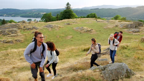 A-multi-ethnic-group-of-five-happy-young-adult-friends-hiking-across-a-field-to-the-summit-during-a-mountain-hike,-close-up