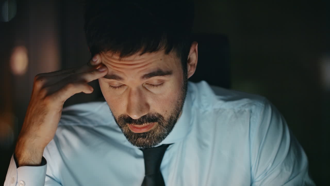 Funcionário desapontado sentado no escritório à noite, sentindo desespero, em close-up. Homem cansado.