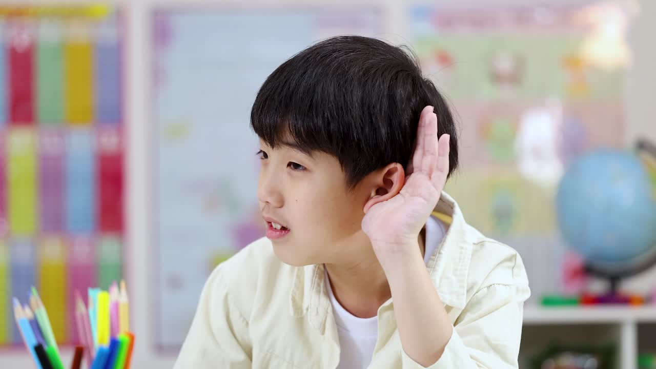 An attentive Asian student cups his ear while listening intently during a classroom lesson