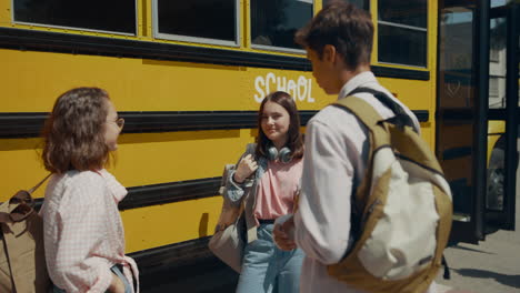 cheerful teen classmates chatting at school bus. friends communicating outdoors