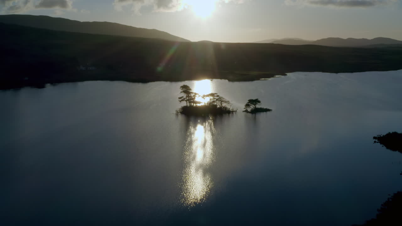 Aerial drone ascend over backlit island in Lough Bofin, the lake’s calm waters and surrounding rugged terrain, Connemara, Galway, Ireland