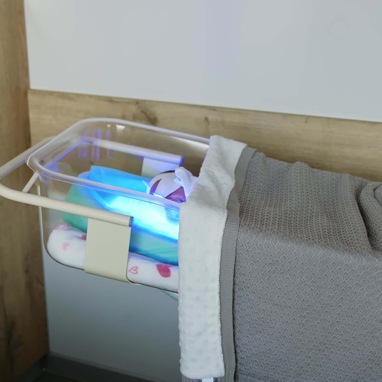 Transparent crib with newborn kid covered with blanket. The baby is cured from jaundice in maternity hospital