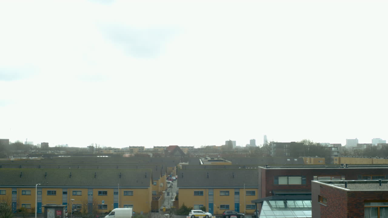 Skyline of a city block in Utrecht. In the distance people walk by and there are cars driving. Occasionally birds fly by. It is a rainy day.